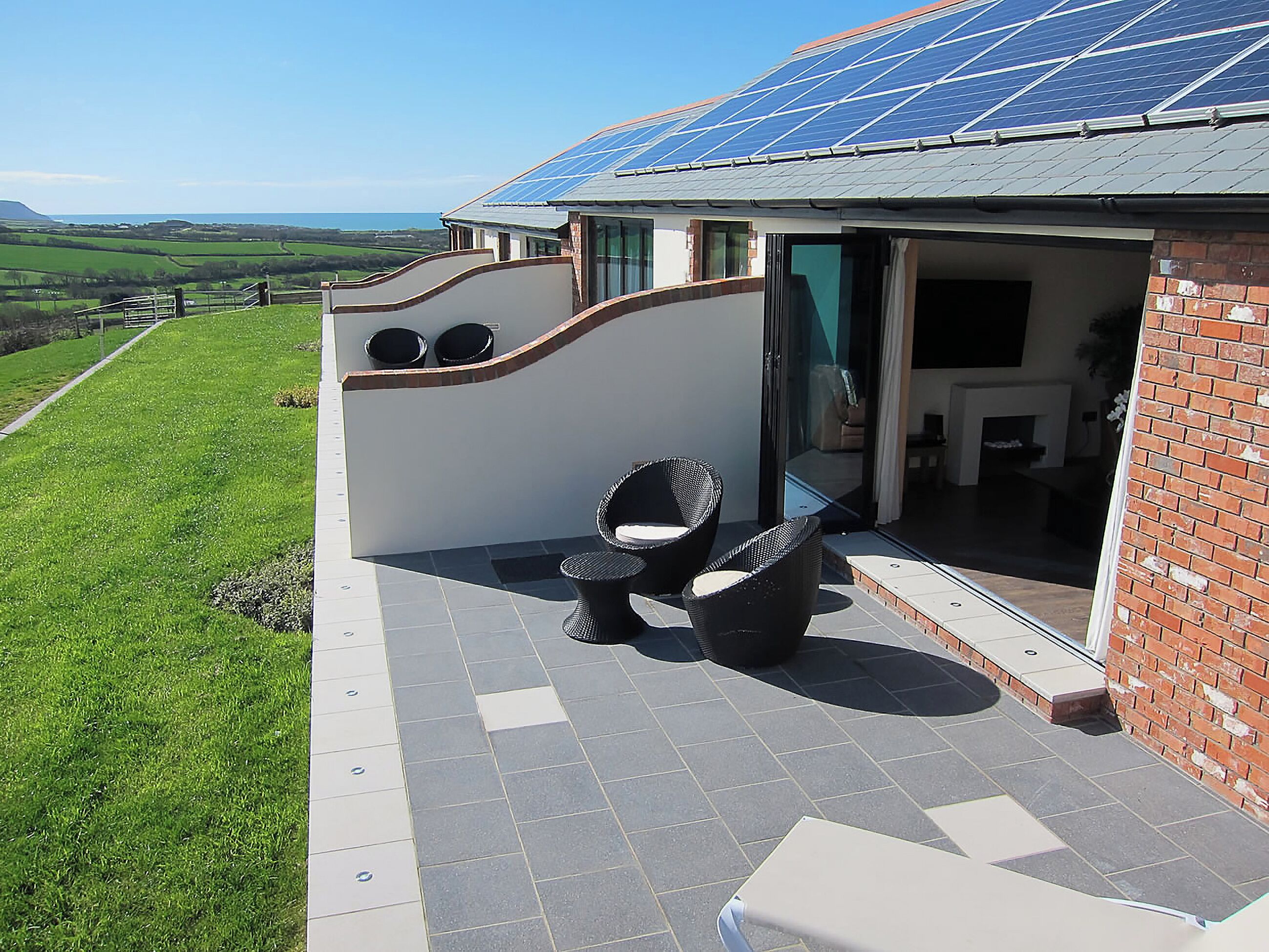 A house with a solar panel roof, a patio with outdoor furniture, and a view of the countryside.