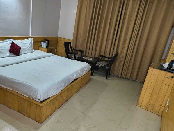 A hotel room with a wooden bed, a small desk, a chair, and a curtain. - Hotel Kasol Inn (Kasol)