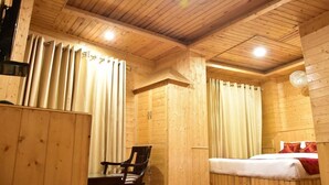 A wooden cabin room with a bed, a chair, and curtains. - Hotel Kasol Inn (Kasol)
