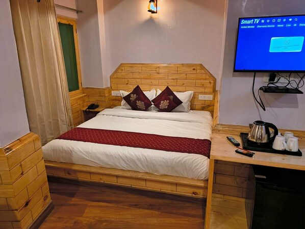 A hotel room with a wooden bed, a TV on the wall, and a coffee station.