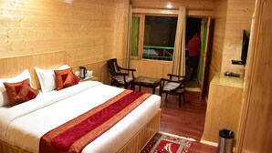 A wooden room with a bed, two chairs, a small table, and a TV. - Hotel Kasol Inn (Kasol)