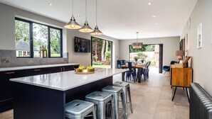 Eine moderne Küche mit einer großen Kochinsel, Barhocker, Pendelleuchten und Blick zum Garten.