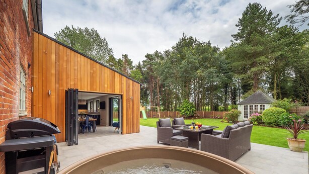 Ein Garten mit Whirlpool, Sitzgelegenheiten im Freien, einer Holzterrasse und einer Ziegelwand.