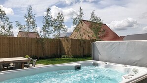 Un jacuzzi con terraza de madera y una mesa con sillas en un jardín trasero.