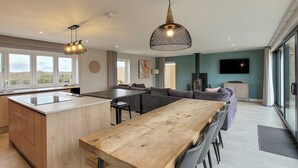 A modern kitchen with a central island, a dining area with a long wooden table, and a living space with a sofa and television. - A stunning luxury holiday home with a swim spa to enjoy too. (Dunholme, near Lincoln)