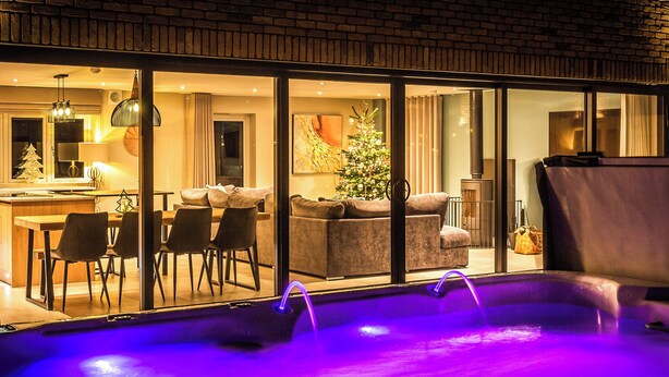 A modern indoor pool with a glass enclosure, a dining area with chairs and a table, and a living room with a sofa and a Christmas tree. - A stunning luxury holiday home with a swim spa to enjoy too. (Dunholme, near Lincoln)