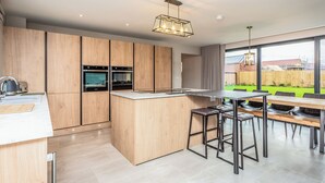 A modern kitchen with wooden cabinets, built-in ovens, a large island, and a dining area with stools.