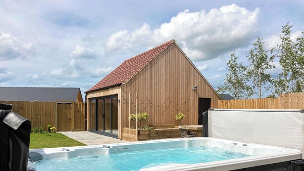 A backyard with a hot tub, a wooden shed, and a fenced area.
