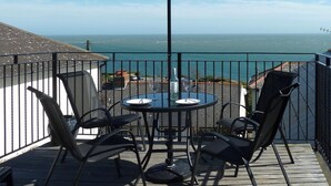 Un balcón con mesa y sillas, un paraguas negro y vista al mar.