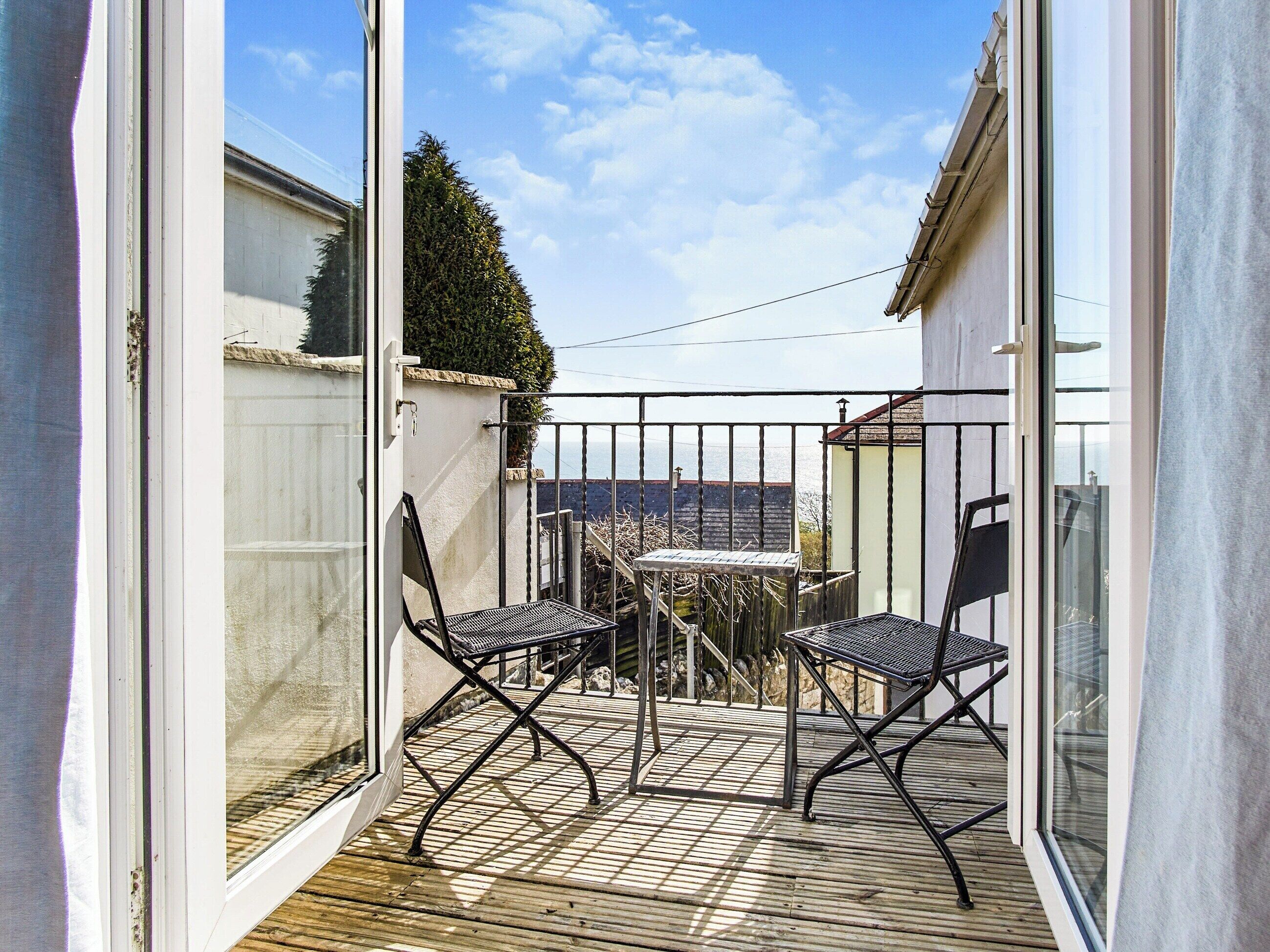 Ein Balkon mit zwei Stühlen und einem kleinen Tisch, mit Blick auf einen Garten und ein Gebäude.