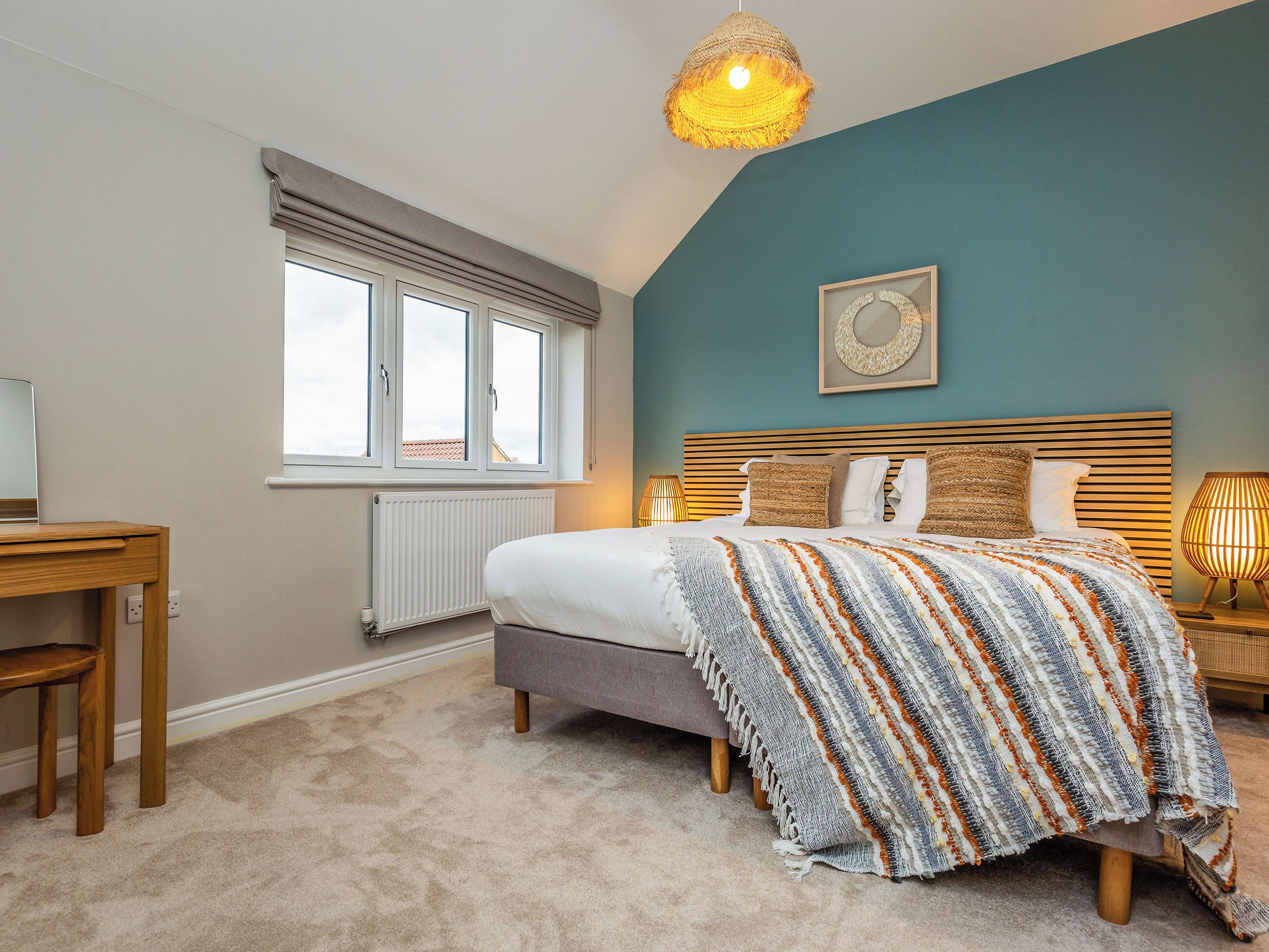 Een slaapkamer met een bed, bureau, raam en een plafondlamp.