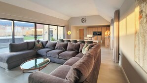 Ein modernes Wohnzimmer mit einer Eckcouch, einem Glastisch und einer Küche im Hintergrund.