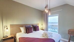 Ein Schlafzimmer mit einem großen Bett, Nachttischlampen, Blick ins Freie und einem Holznachttisch.