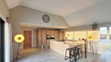 A modern kitchen with a central island, pendant lighting, and a clock on the wall.