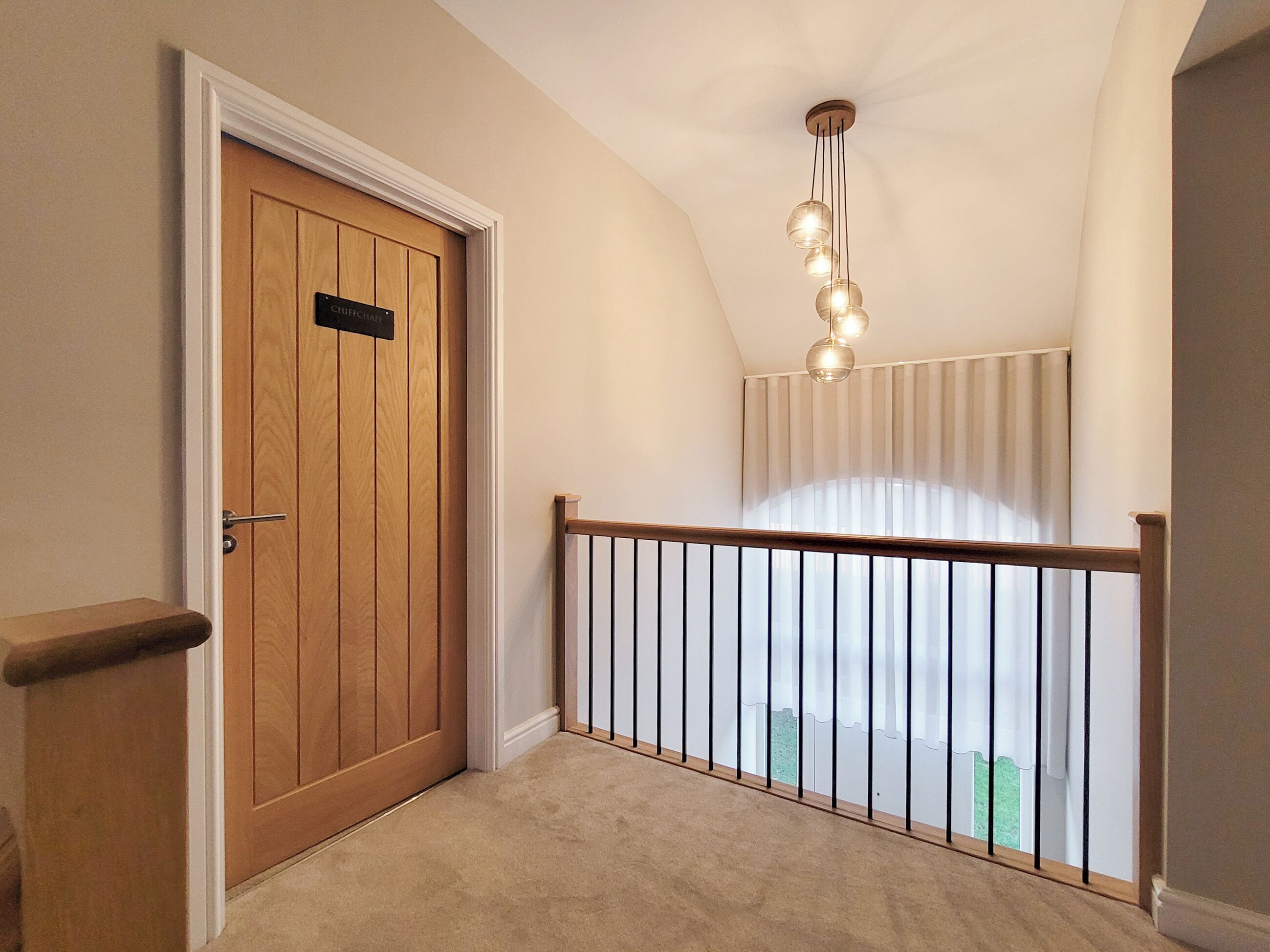 Un couloir avec une porte en bois, un luminaire au plafond et une vue par une fenêtre avec des rideaux.