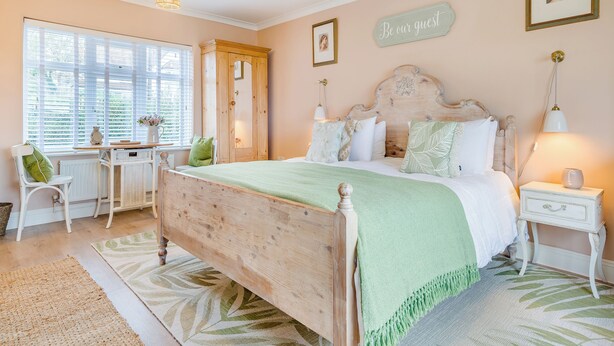 A bedroom with a wooden bed, a desk with a chair, a window with blinds, and a wall sign. - 1 bedroom accommodation in Blue Anchor, near Minehead (Blue Anchor, near Minehead)