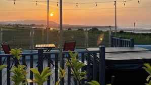 An outdoor seating area with a view of the sunset over the ocean, string lights, and a wooden deck. - 1 bedroom accommodation in Blue Anchor, near Minehead (Blue Anchor, near Minehead)