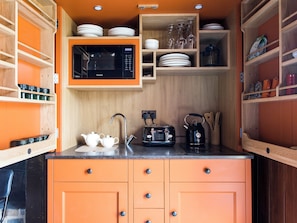 Una cocina compacta equipada con microondas, tostadora, hervidor y diferentes utensilios.