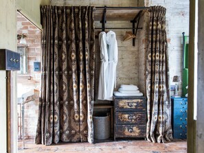 Un baño rústico con cortinas estampadas, una bata colgada, un aparador de madera y una lámpara de metal.