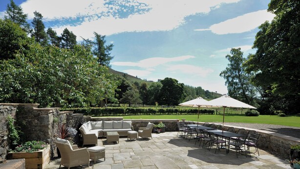 Eine Terrasse mit Steinbelag, Gartenmöbeln und Sonnenschirmen.