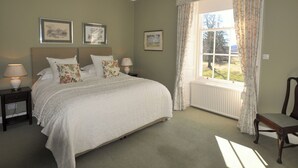 Ein Schlafzimmer mit einem Bett, zwei Nachttischen, einem Sessel, einem Fenster mit Vorhängen und gerahmten Bildern an der Wand.