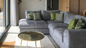 Un sofá seccional gris con varios cojines, una mesa redonda con patas doradas y un adorno circular grande en la pared.
