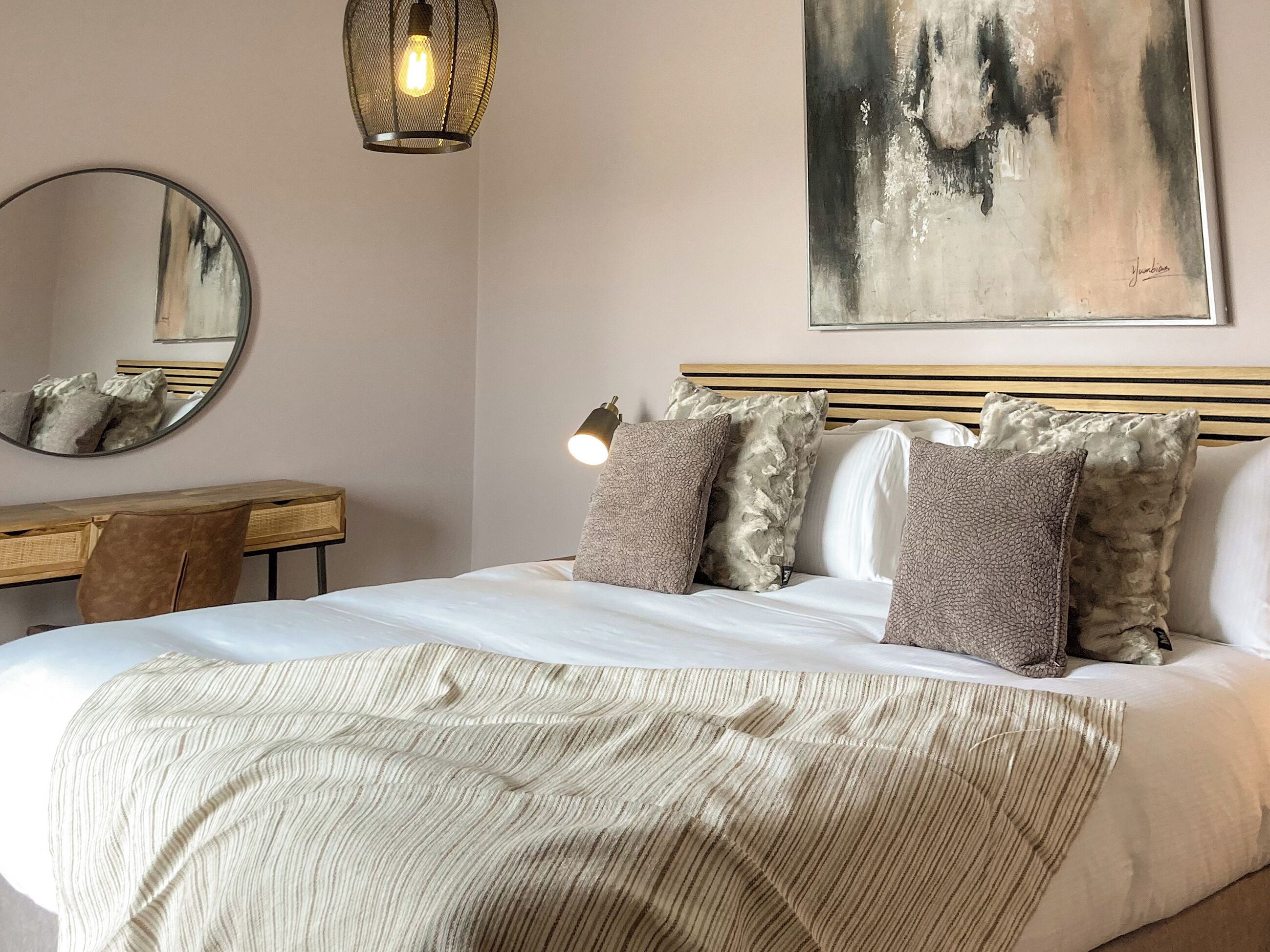 Een slaapkamer met een bed, een bureau, een stoel, een hanglamp en een schilderij aan de muur.