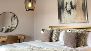 Un dormitorio con cama, escritorio, silla, lámpara colgante y un cuadro en la pared.