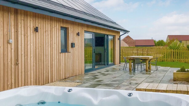 Una casa de madera con un patio, un jacuzzi y una cerca de madera al fondo.
