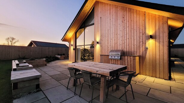 Eine Terrasse im Freien mit einem Holztisch und -stühlen, einem Grill und einem Holzzaun.