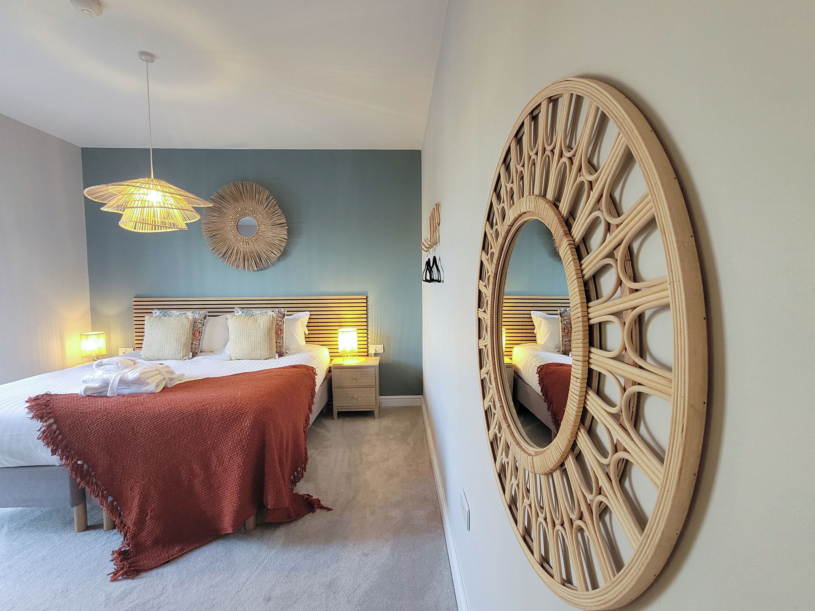 Un dormitorio con cama, mesitas de noche, un espejo en la pared y una lámpara colgante.