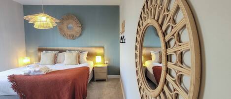 A bedroom with a bed, bedside tables, a wall mirror, and a hanging light fixture.