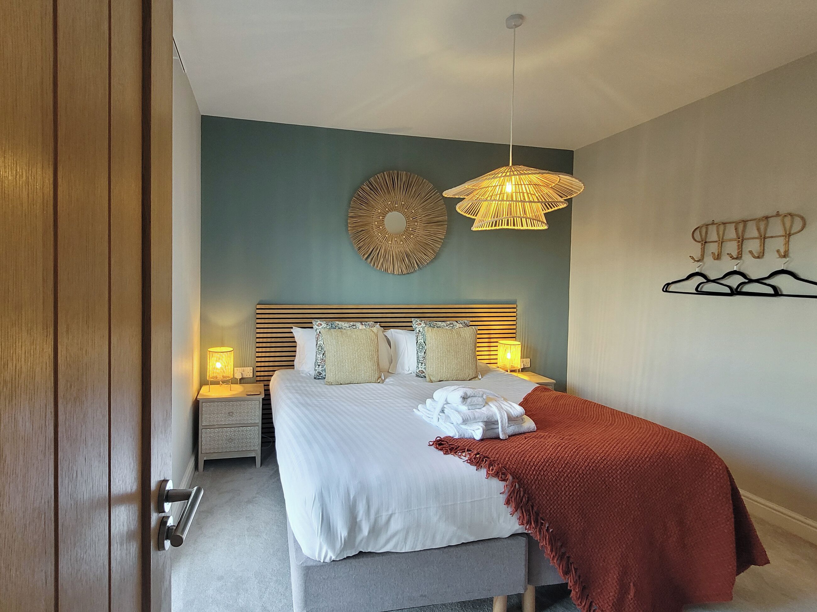 A neatly made bed with a white and red blanket, a bedside lamp, and a wall-mounted decorative item.