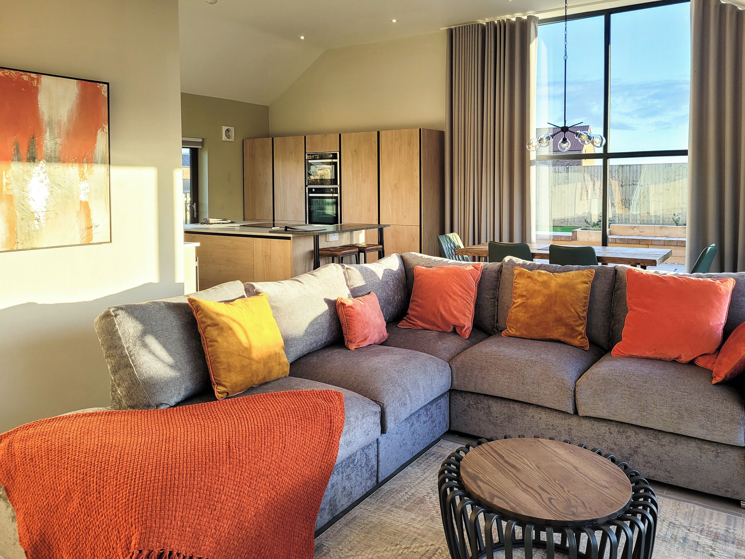 A modern living room with a sectional sofa, a round wooden table, and a kitchen in the background.