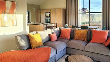 A modern living room with a sectional sofa, a round wooden table, and a kitchen in the background.