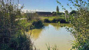 A pond surrounded by greenery, a building in the background, and a clear sky. - Bailgate Barn - UKC4646 (Dunholme, near Lincoln)