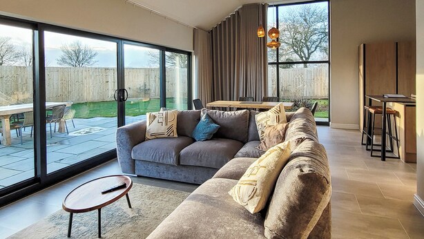 A modern living room with a sofa, a dining table, and large windows. - Bailgate Barn - UKC4646 (Dunholme, near Lincoln)