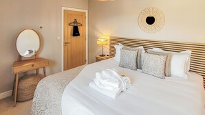 A hotel room with a bed, a bedside table, a mirror, a hanging towel rack, and a wall-mounted lamp. - Bailgate Barn - UKC4646 (Dunholme, near Lincoln)