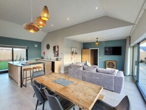 A modern kitchen with a central island, a dining area with a wooden table, and a living space with a grey sofa. - Bailgate Barn - UKC4646 (Dunholme, near Lincoln)