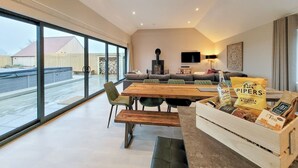 Een ruime woonkamer met een groot raam, een houten eettafel, een bank en een televisie.