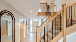 Un hall d’entrée spacieux avec un escalier en bois, un grand miroir et un extincteur.