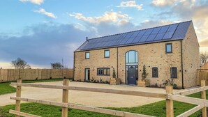 Une maison à deux étages, construite en briques, avec un toit équipé de panneaux solaires, une porte d’entrée et une allée bordée d’une clôture.