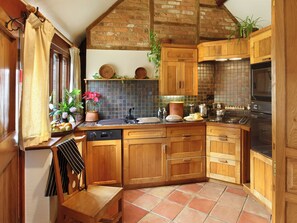 A kitchen with wooden cabinets, a tiled backsplash, and a brick ceiling. - Hazelnut Cottage - UKC4656 (Swerford, near Chipping Norton)