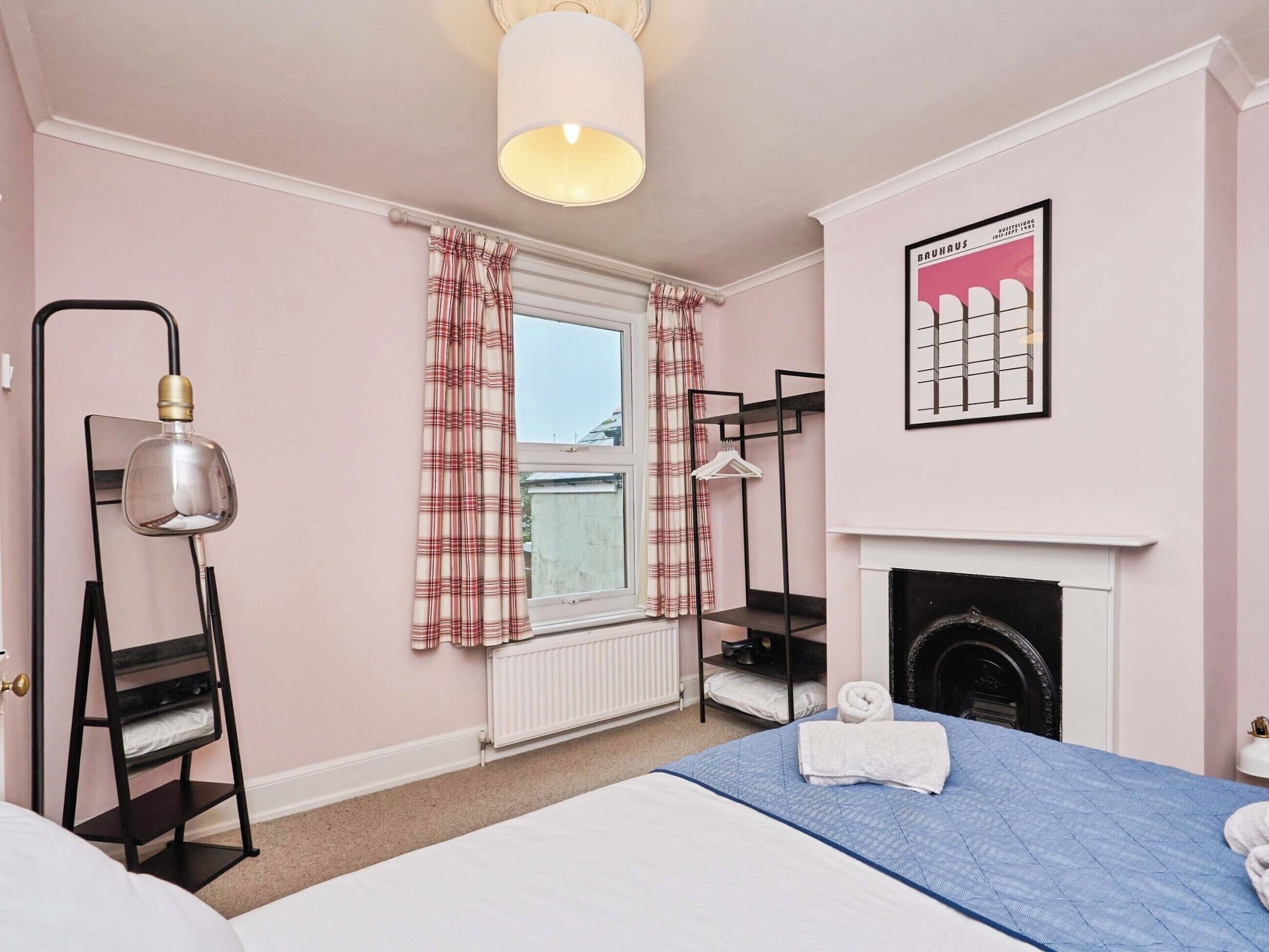A bedroom with a bed, a radiator, a fireplace, a hanging lamp, and a window with curtains.