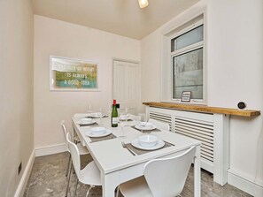 A dining room with a white table set for four, a wine bottle, and a framed quote on the wall. - 3 bedroom accommodation in Cowes (Cowes)