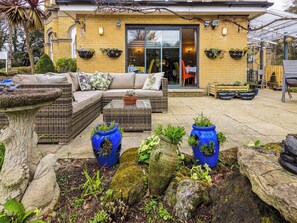 A cozy outdoor seating area with wicker furniture, potted plants, and a stone birdbath. - 5 bedroom accommodation in Shanklin (Shanklin)
