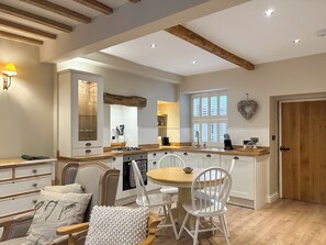 A modern kitchen with white cabinetry, wooden beams, a central island, and a dining area with white chairs. - 3 bedroom accommodation in Skipton (Skipton)