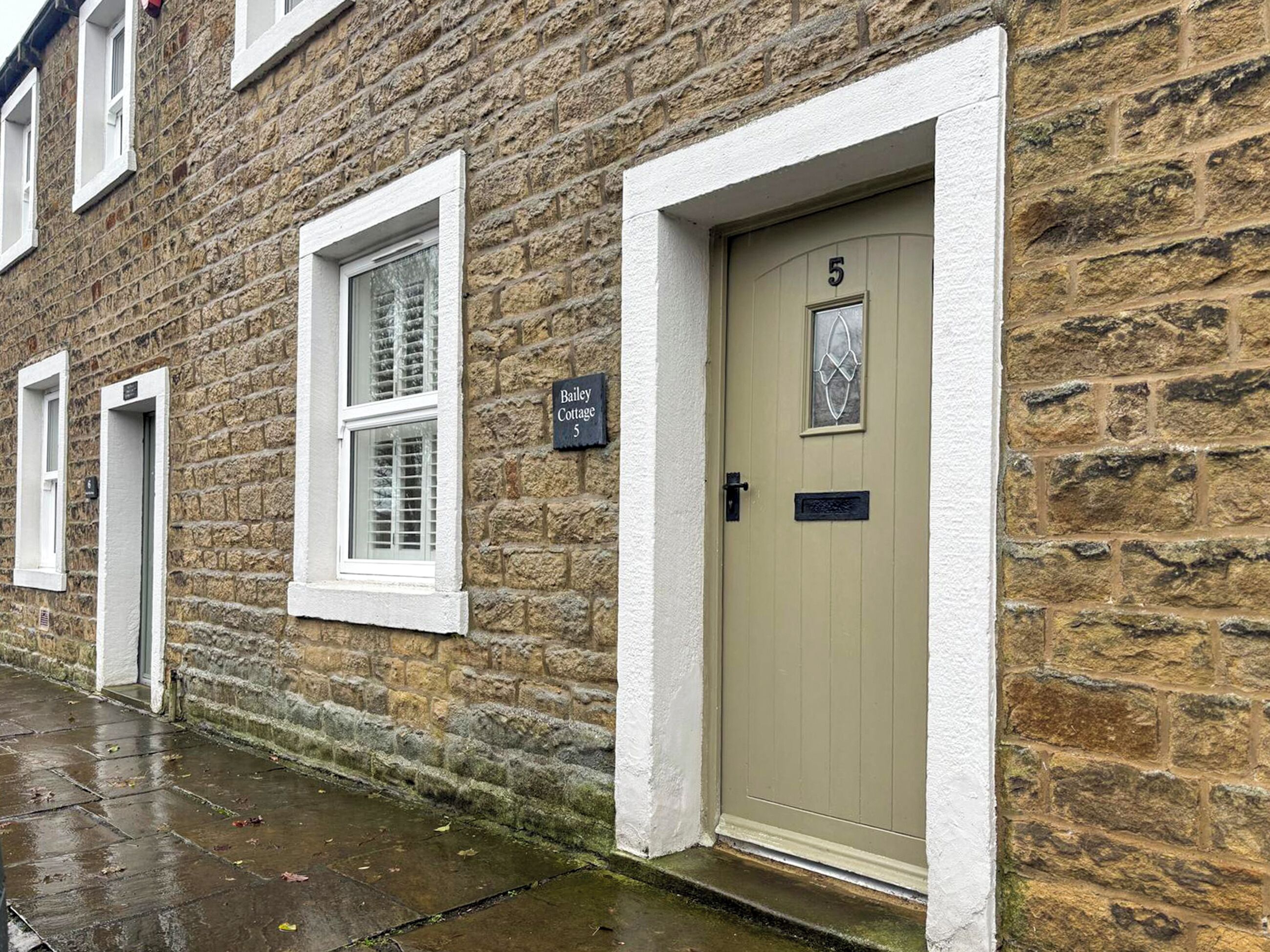 Un bâtiment en pierre avec une porte beige portant l’inscription « Bailey Cottage 5 ».