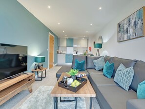 Ein modernes Wohnzimmer mit Fernseher, Sofa, Couchtisch und einer Küche im Hintergrund.