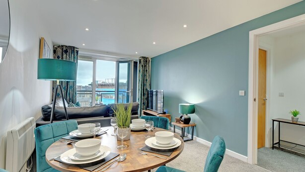 A dining area with a round table set for four, surrounded by teal upholstered chairs. - All Saints Apartments 4A (Newcastle Upon Tyne)